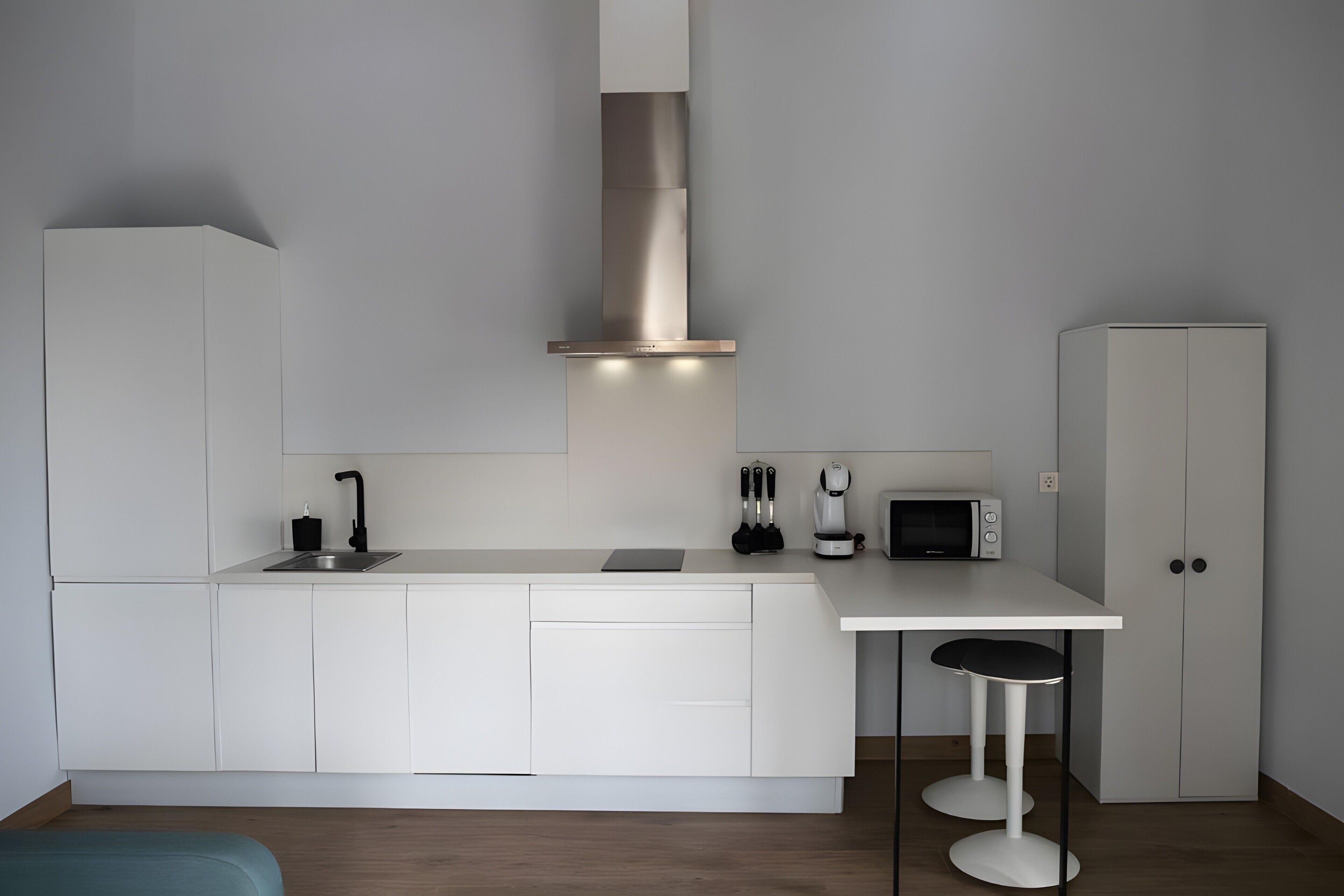 Een moderne keuken met witte kasten, een roestvrijstalen afzuigkap, een magnetron en een koffieapparaat.