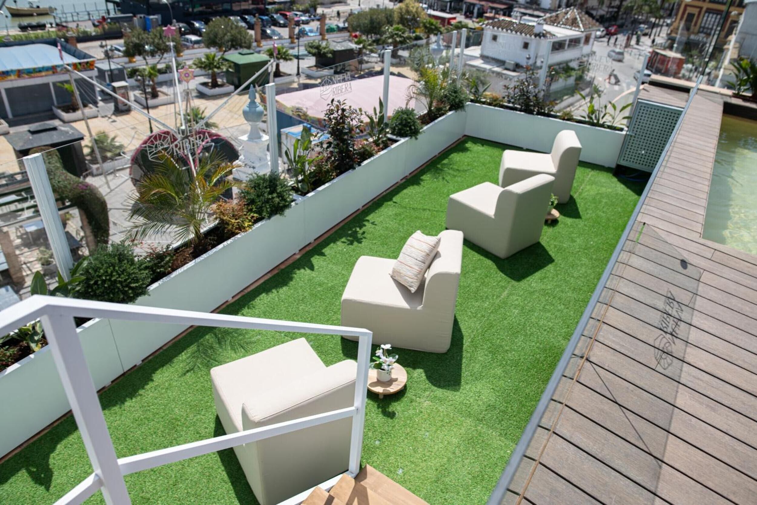 Una terraza en la azotea con césped artificial, mobiliario exterior blanco y vistas a la ciudad.