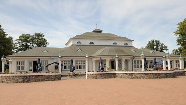 A large building with a central dome and multiple windows, surrounded by a paved area with outdoor seating and umbrellas. - Holiday apartment with 2 bedrooms (Ueckermünde)