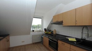 A kitchen with wooden cabinets, a black countertop, a window, and a view of trees outside. - Holiday apartment with 2 bedrooms (Ueckermünde)