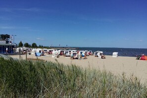 Ein Strand mit Reihen von Liegestühlen und Sonnenschirmen, ein Steg im Hintergrund und ein klarer Himmel.