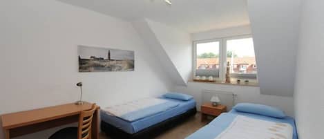 A bedroom with two single beds, a desk, and a chair.