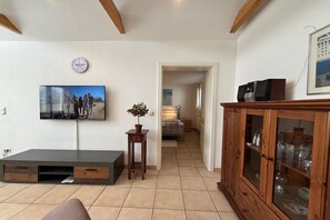 A living room with a flat-screen TV, a wooden cabinet with glass doors, and a small table with a potted plant. - Holiday home with 1 bedroom (Travemünde)