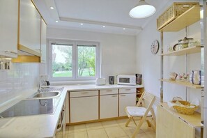 Een moderne keuken met witte kasten, een magnetron, een spoelbak en een raam met uitzicht op groen.