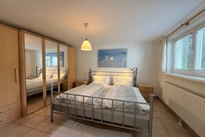 A bedroom with a bed, bedside tables, a wardrobe, a window with blinds, and a painting on the wall. - Holiday home with 1 bedroom (Travemünde)
