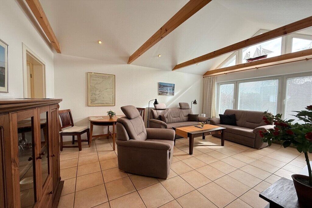 Ein geräumiges Wohnzimmer mit hoher Decke, Holzbalken, einer Sofagarnitur, einem Couchtisch und einem Essbereich mit Stühlen und einem Tisch.