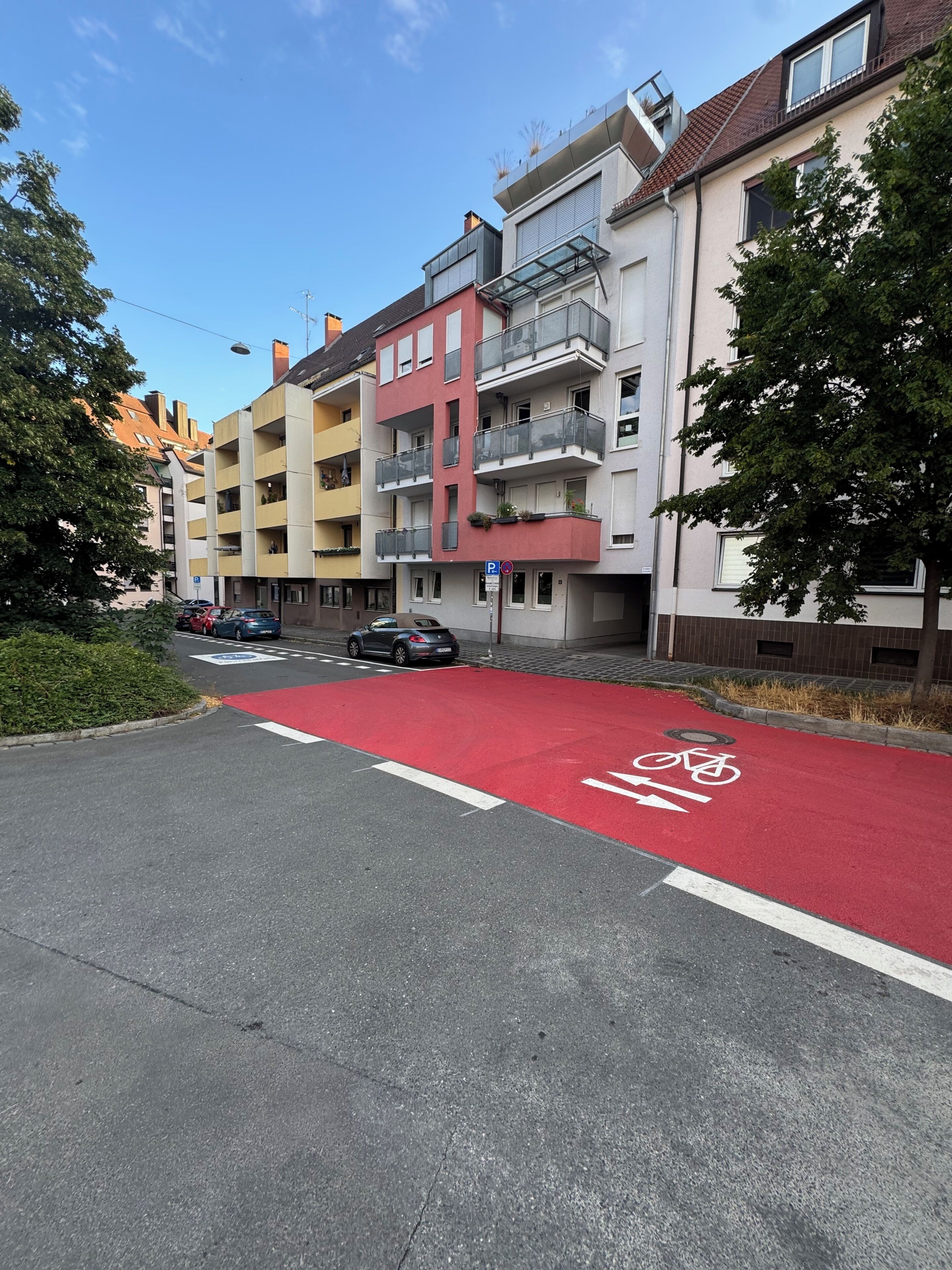 En gata med en röd cykelbana, parkerade bilar och flerfamiljshus.
