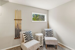 Ein Zimmer mit zwei Polsterstühlen, einem kleinen Beistelltisch und einem an der Wand befestigten Poolbillardständer.