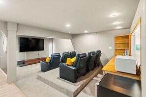 Ein Heimkino mit Flachbildfernseher, Liegesesseln, einem Holztisch und einer festen Regalanlage.