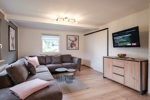 Ein modernes Wohnzimmer mit einem Ecksofa, einem Couchtisch, einem Schrank und einem an der Wand befestigten Flachbildfernseher.