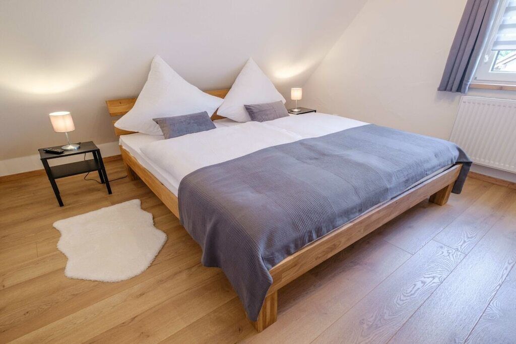 A bedroom with a wooden bed, white bedding, a white rug, and two bedside lamps.