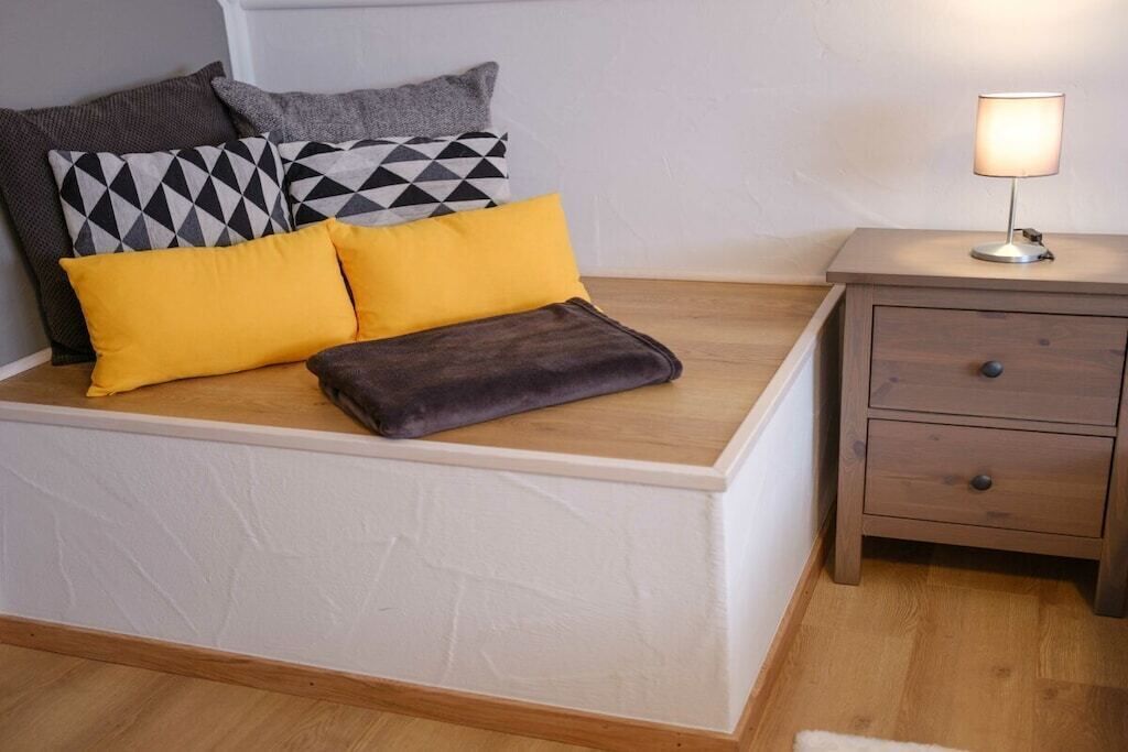 Een bed met een houten hoofdbord, een nachtkastje met een lamp, en een bijzetmeubel met lades.