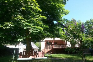 A residential area with a large tree, a swing set, and a building with a balcony. - Holiday home with 2 bedrooms (Heidesee OT Bindow)