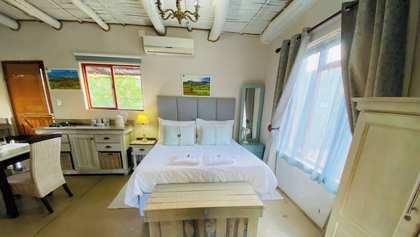 A bedroom with a bed, bedside table, lamp, and a view of the outdoors through a window.