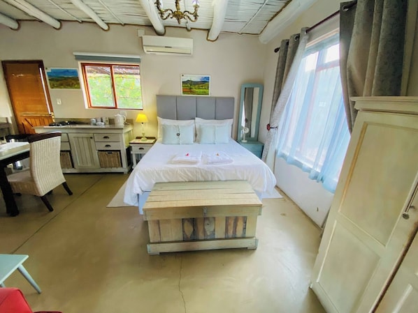 A bedroom with a bed, bedside table, lamp, and a view of the outdoors through a window.