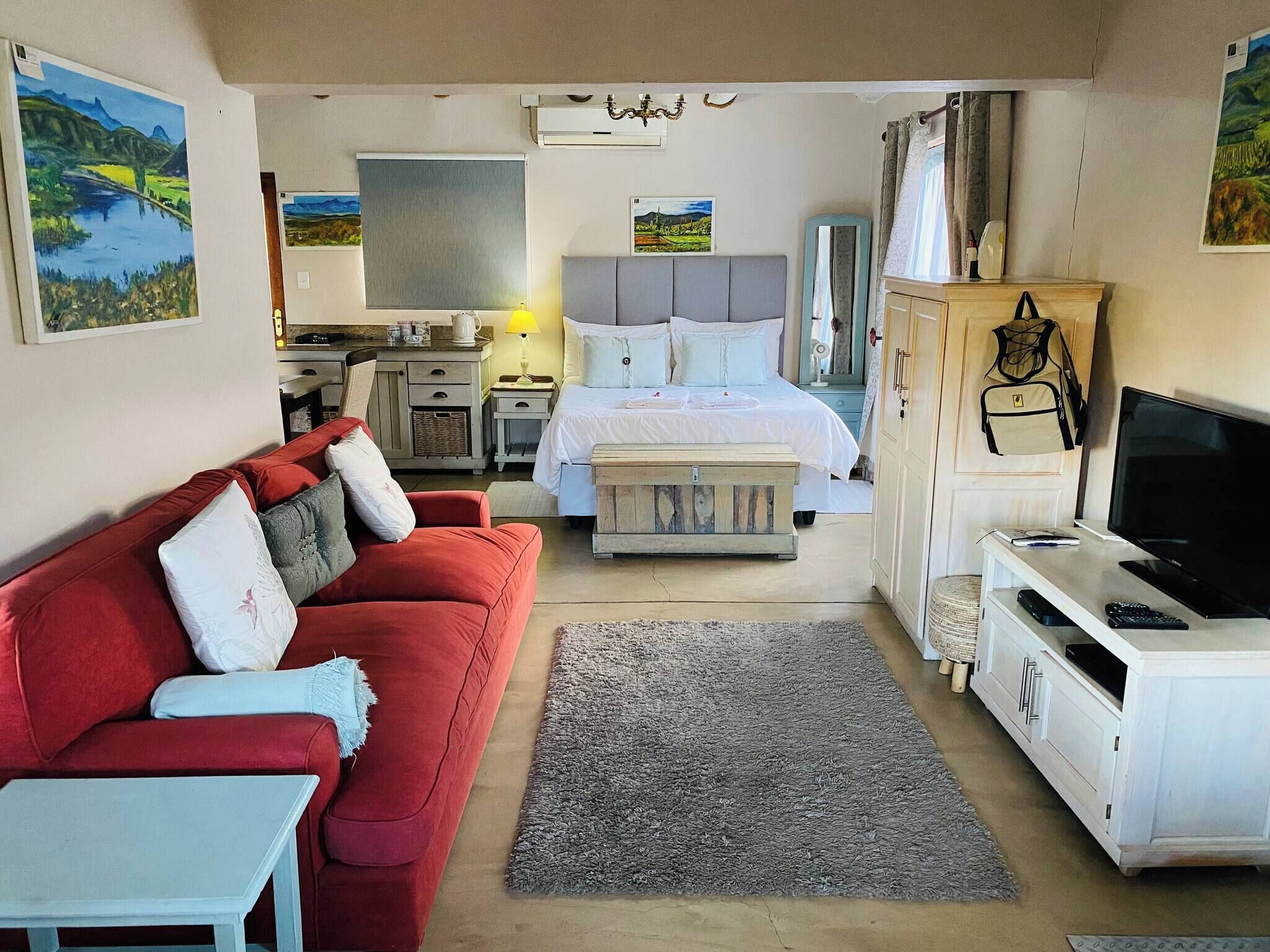 Una habitación de hotel con una cama, un sofá rojo, una televisión y un escritorio.
