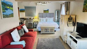 Quarto de hotel com uma cama, um sofá vermelho, uma televisão e uma escrivaninha.