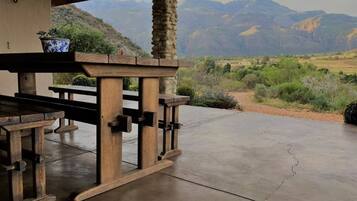 Un patio exterior con un pilar de piedra, una mesa de madera y bancos, con vistas a un paisaje montañoso.
