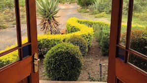 An open wooden door leading to a landscaped garden with a view of rolling hills and a clear sky.