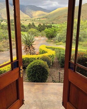 An open wooden door leading to a landscaped garden with a view of rolling hills and a clear sky.