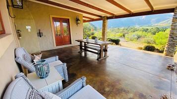 Un patio cubierto con una mesa y sillas de madera, un pilar de piedra y vistas a un paisaje montañoso.