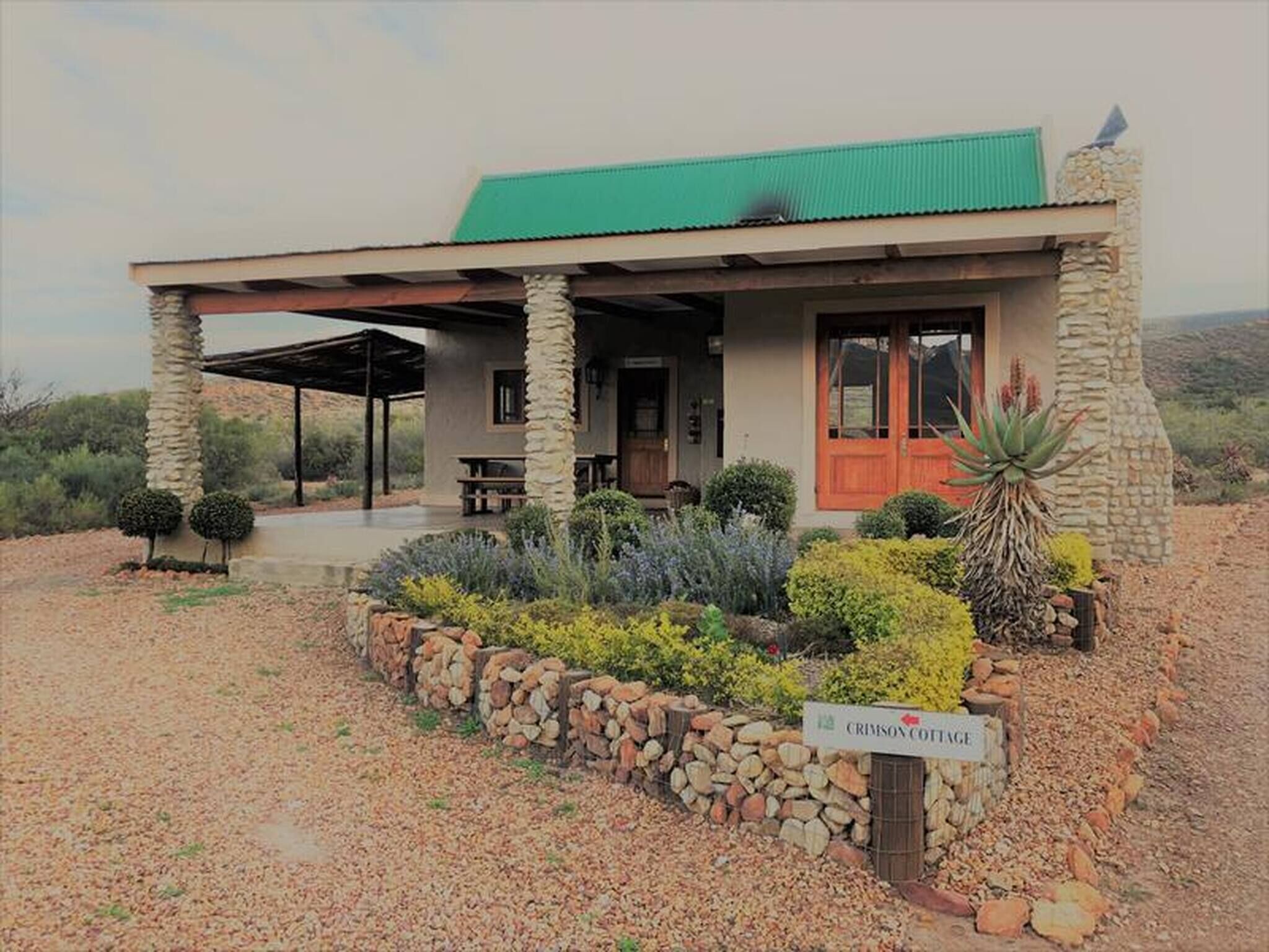 Un edificio rústico de piedra con techo verde, un porche cubierto y un letrero que dice 'CRIMSON COTTAGE'.