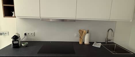 A modern kitchen with white cabinets, a black countertop, a built-in oven, and a stainless steel sink.