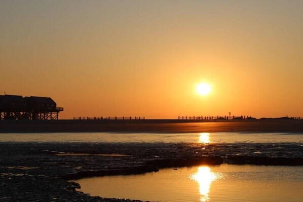 A sunset over a beach with a pier extending into the water. - Holiday home with 3 bedrooms (St.Peter-Ording)