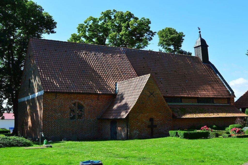 A brick building with a steeply pitched roof and a small tower with a cross on top.