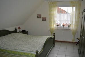 Een slaapkamer met een bed, een raam met gordijnen, een radiator en een klein nachtkastje met een lamp.