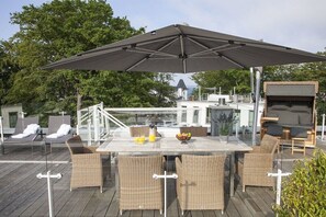 An outdoor deck with a table and chairs, a large umbrella, and lounge chairs. - Paradise Cloud at Villa Augustine (Ostseebad Binz)