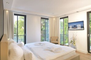A hotel room with a large bed, a chair, a television, and a view of the outdoors. - Paradise Cloud at Villa Augustine (Ostseebad Binz)
