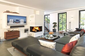 A modern living room with a fireplace, a large flat-screen TV, and a comfortable sofa. - Paradise Cloud at Villa Augustine (Ostseebad Binz)