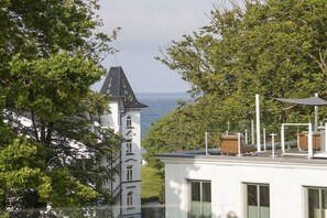 A white building with a tower, a view of the sea, and trees in the foreground. - Paradise Cloud at Villa Augustine (Ostseebad Binz)