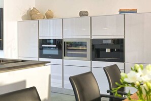 A modern kitchen with built-in appliances, a dining area with chairs, and a decorative vase on the wall. - Paradise Cloud at Villa Augustine (Ostseebad Binz)