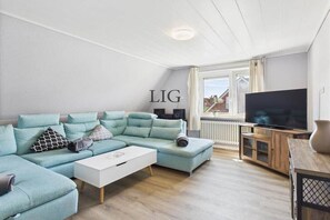 Een moderne woonkamer met een hoekbank, een flatscreen televisie en een houten kast.