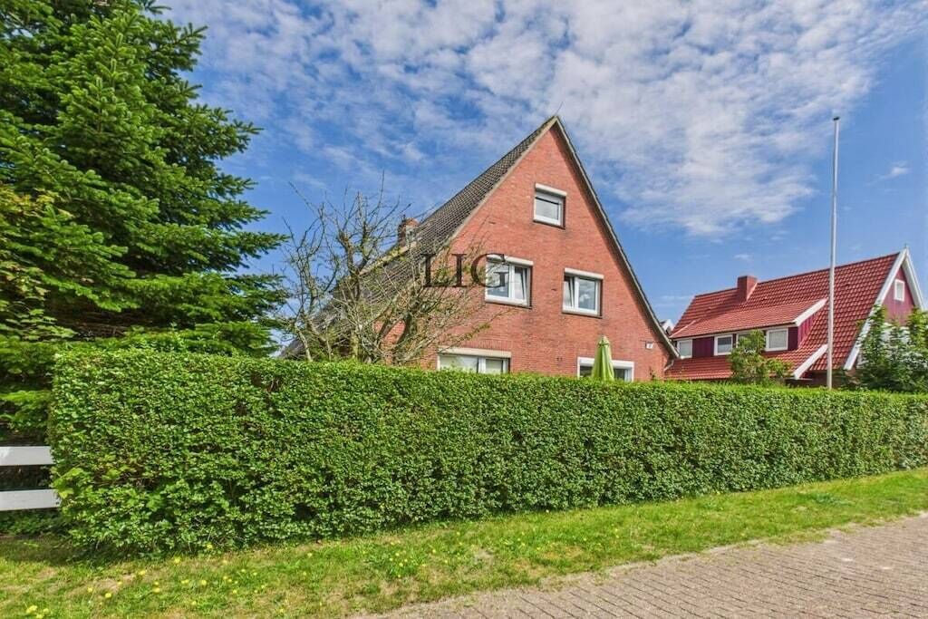 A red-brick house with a triangular roof, a hedge in the foreground, and a clear blue sky.