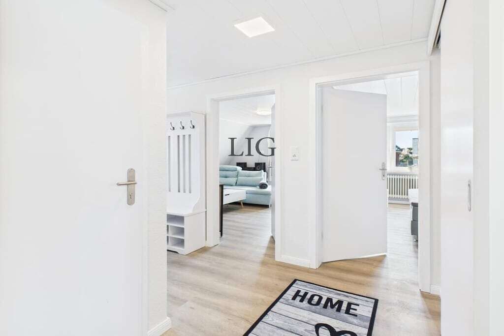 A modern interior with a hallway leading to a living area, a visible 'HOME' mat, and a 'LIG' sign.