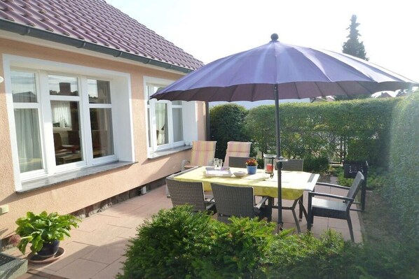 Un patio con tavolo e sedie, un ombrellone viola e una casa con tetto in tegole.
