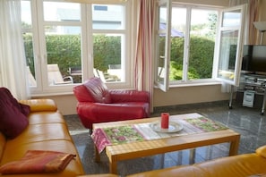 Ein Wohnzimmer mit einer Couch, einem roten Sessel, einem Tisch mit Untersetzer und einem Fernseher.