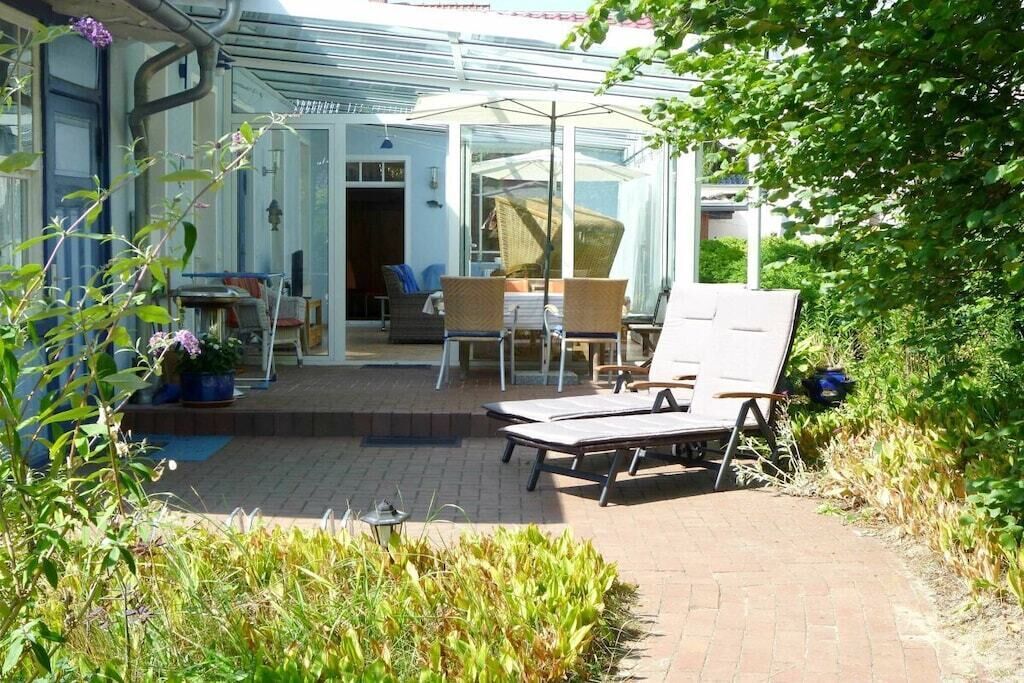 A sunlit patio with outdoor furniture, a glass door leading to a room, and a garden area.