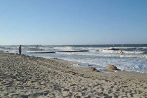 Ein Strand mit einem Pier im Hintergrund, sandigem Ufer und Wellen.
