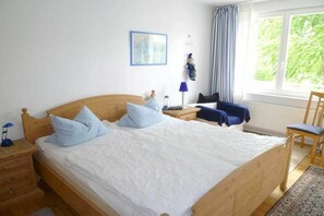 A bedroom with a wooden bed, a nightstand, a chair, a window with curtains, and a framed picture on the wall. - Villa Romantica OG - with conservatory (Koserow)