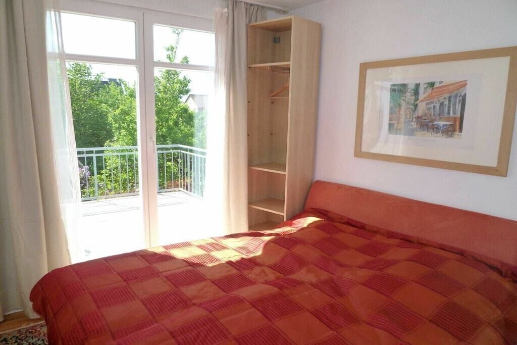A bedroom with a bed, a wardrobe, a balcony, and a framed picture on the wall.