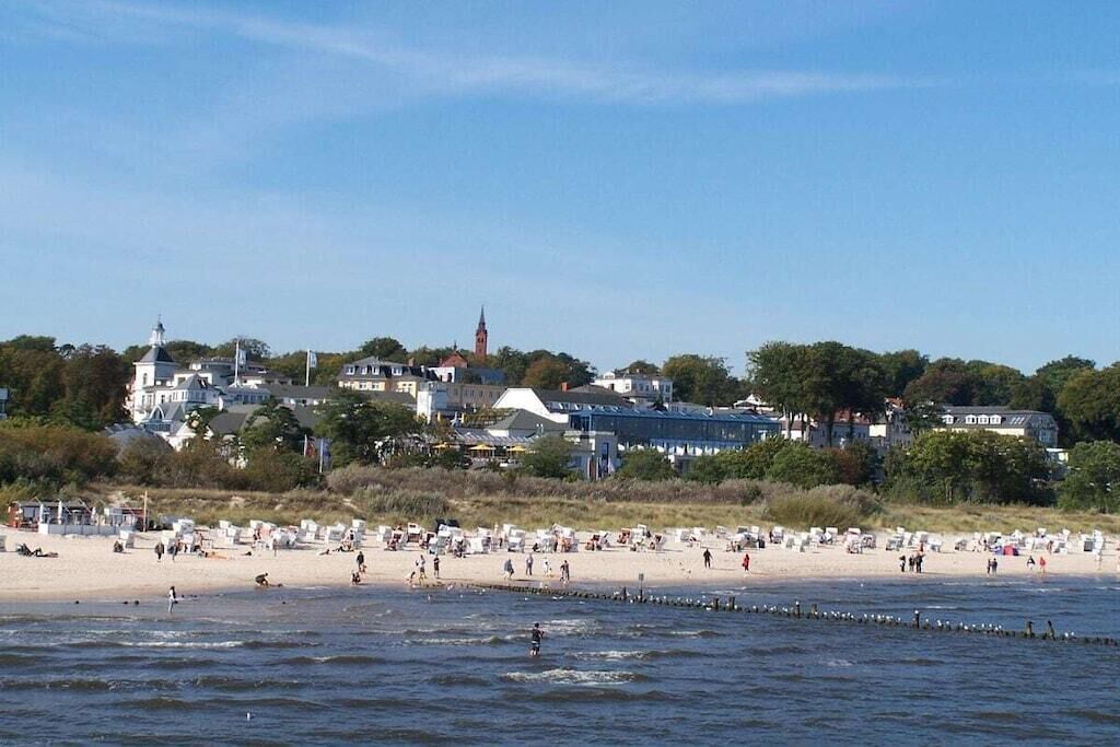 A beach with people, a pier, and buildings in the background.