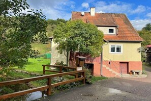 A two-story house with a red-tiled roof, a small window, and a wooden fence. - Holiday home at Krechenbach (Eckarts)