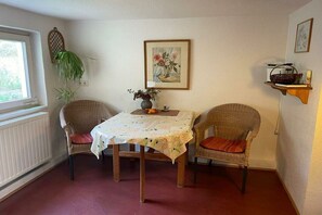 A dining area with two wicker chairs, a table with a floral tablecloth, a vase with flowers, and a painting on the wall. - Holiday home at Krechenbach (Eckarts)