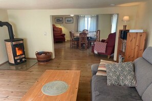 A cozy living room with a wood-burning stove, a dining area with chairs, and a sofa with a patterned cushion. - Holiday home at Krechenbach (Eckarts)