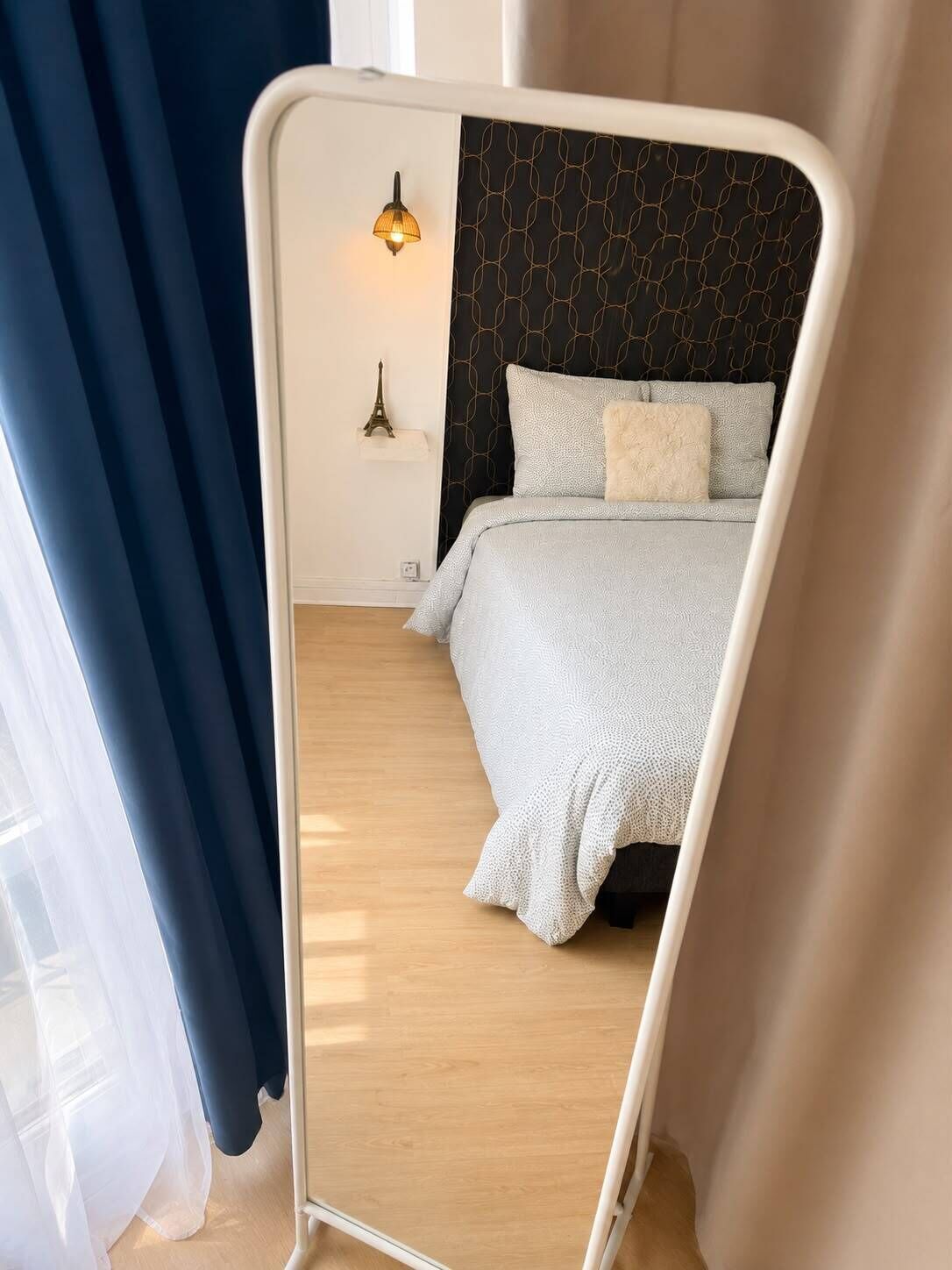 Un dormitorio con una cama, una mesita de noche, una lámpara de pared y una Torre Eiffel decorativa.