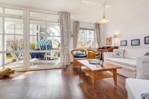 Ein großzügiger Wohnbereich mit einer Schiebetür zum Balkon, einem weißen Sofa, einem Holztisch und einem Korbstuhl.